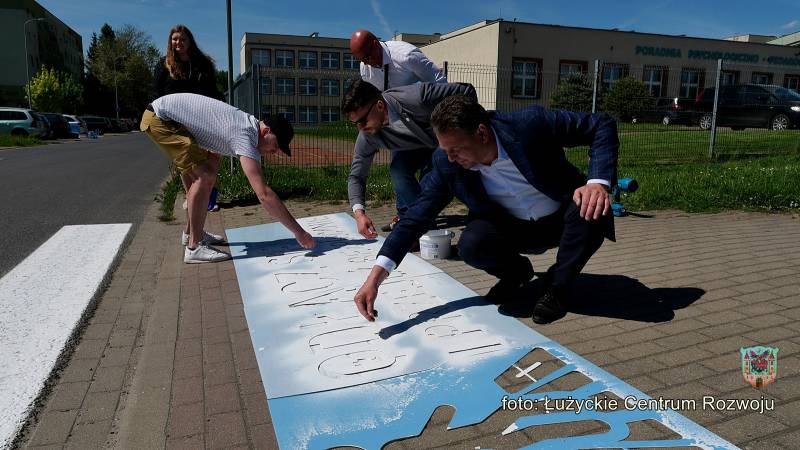 mężczyźni (na pierwszym planie burmistrz) wykonują napis na chodniku